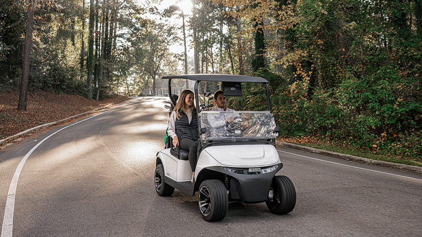 Two people riding in an E-Z-GO vehicle down a road in a scenic forest 