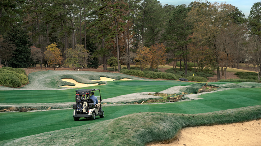 An E-Z-GO golf cart driving through the fairway with a bagwell on the back.