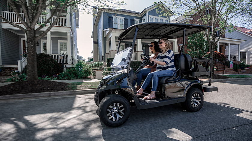 Two women drive an E-Z-GO down the street.