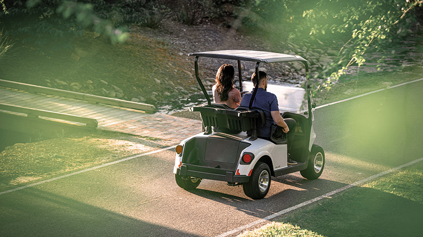 Two individuals driving an E-Z-GO from behind