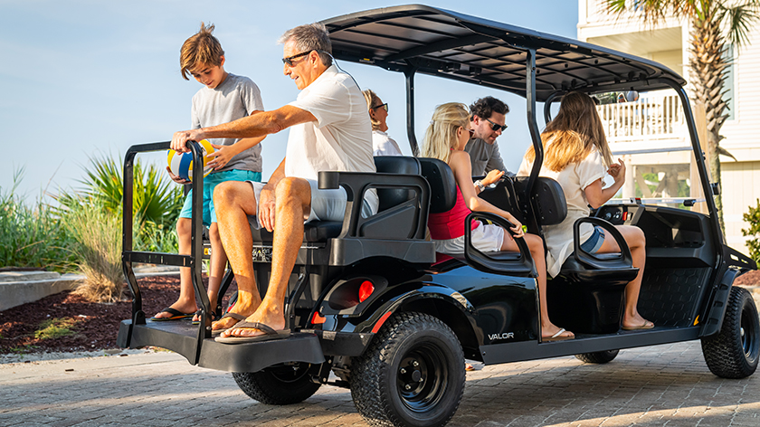 A large family of 6 sitting in an E-Z-GO Valor 6 golf cart.