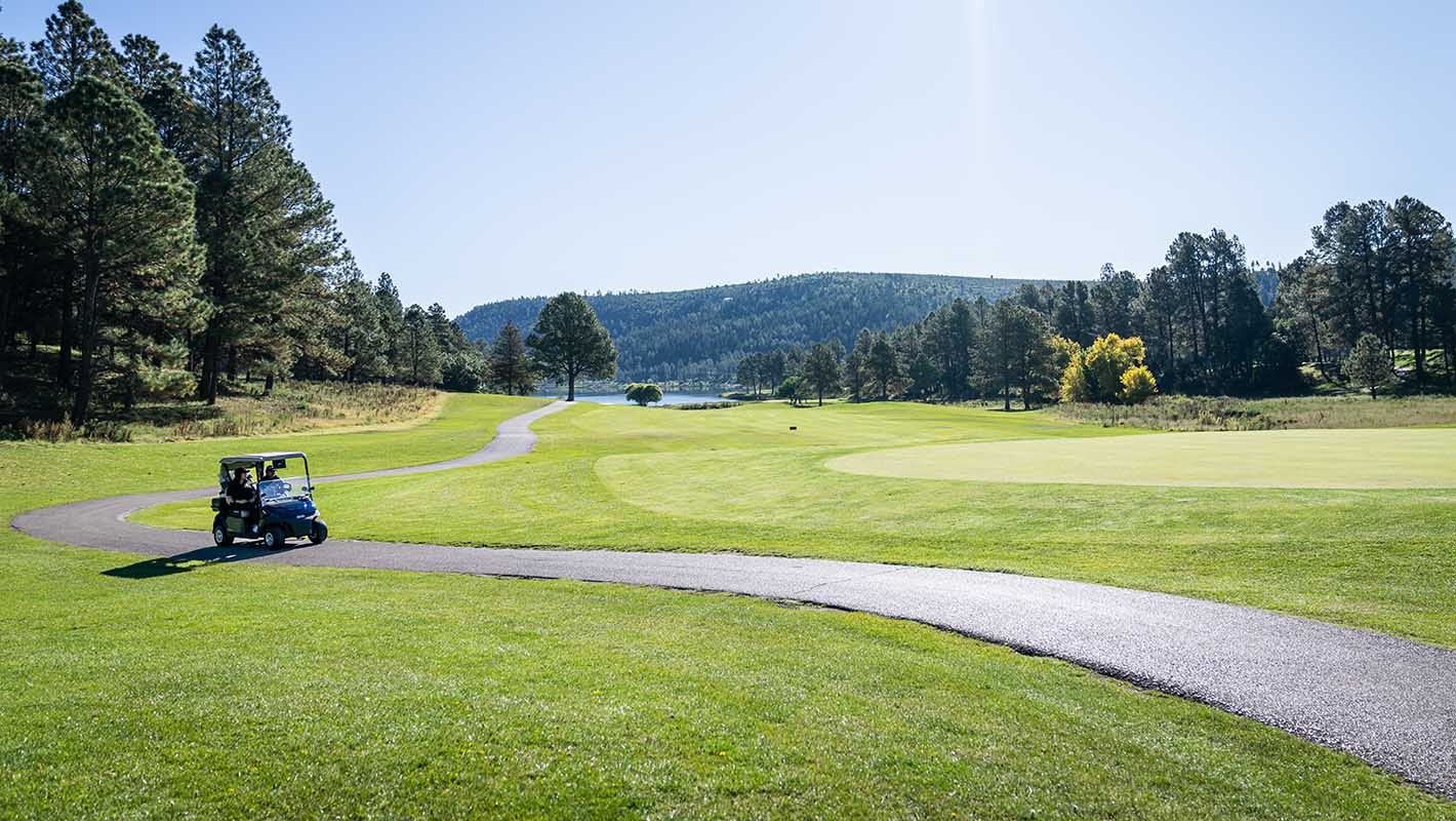 An E-Z-GO golf cart driving down a golf cart pathway.