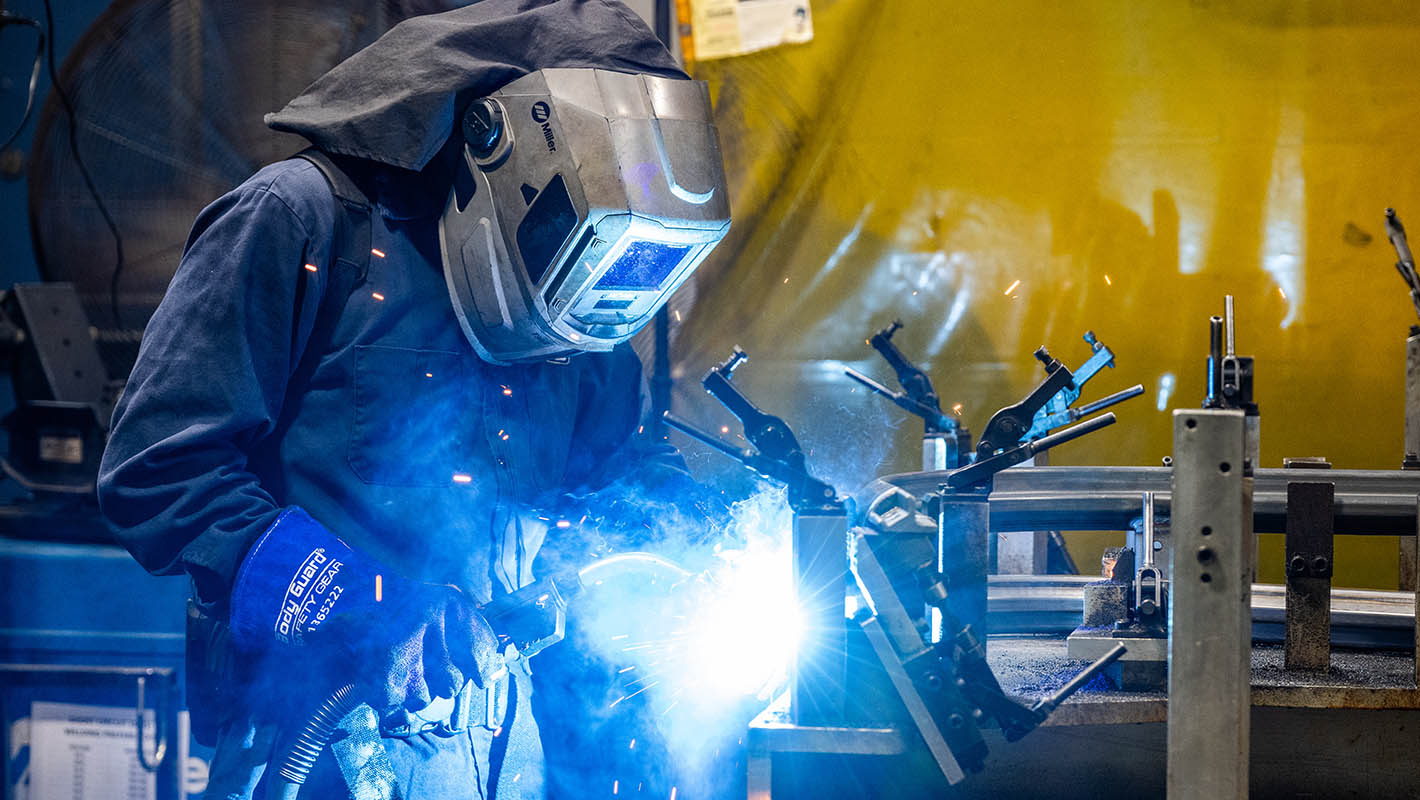 A person wearing full welding gear welding metal together.