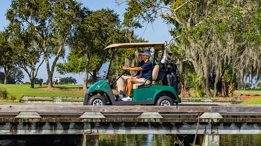 Two golfers riding in an RXV ELiTE across a bridge and pond on a golf course.
