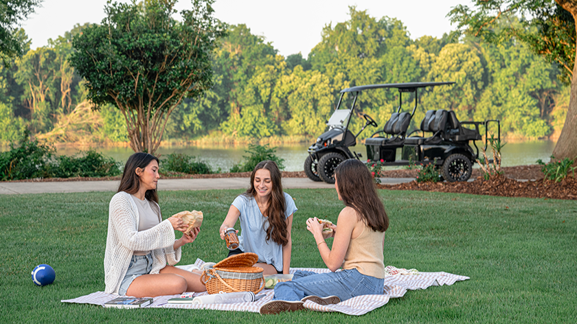 Family having a picnic in the park with river and E-Z-GO Express 6 in the background